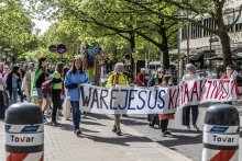 Menschen gehen beim Protestmarsch mit dem langen Banner mit der Aufschrift "Wäre Jesus Klimaaktivist" einer großen Menge voran